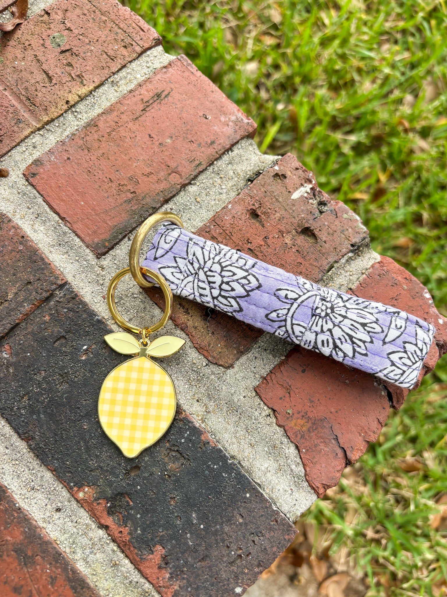 Keychain with lemon charm and floral-patterned strap on a brick surface